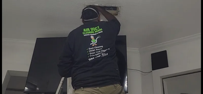 Real Air Duct Cleaning Miami technician in branded black shirt cleaning ducts in Hollywood FL home
